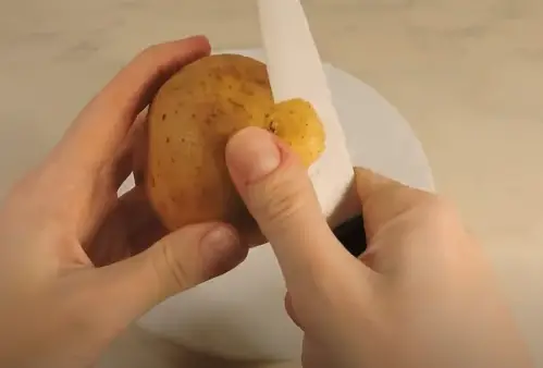 Cutting Off Small Bits Of Skin With Knife Cut off small bits of skin from the potato with a sharp paring knife.