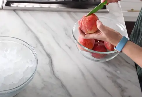 Make a half-centimeter deep 'X' on the pointy side of each peach with a knife Make a half-centimeter deep 'X'