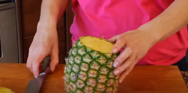 Stand the pineapple up and slice it straight down the center, Stand the pineapple up